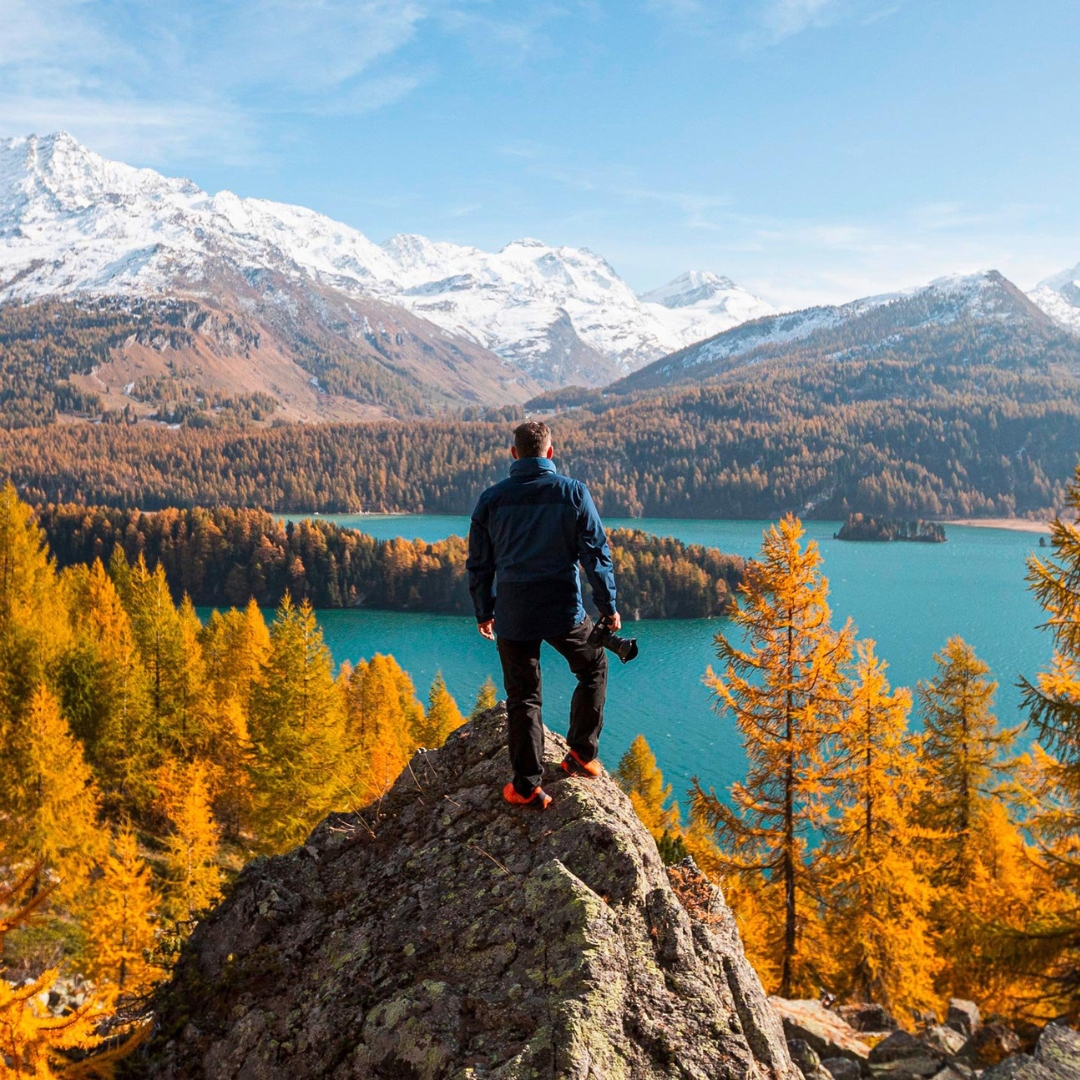 adventurer on a mountain in Switzerland with a camera in front of a fall landscape